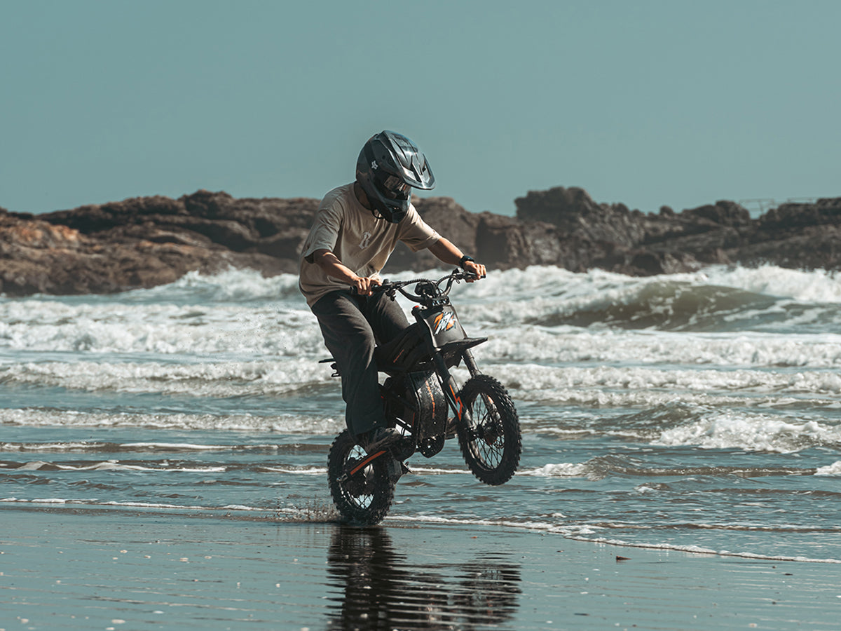 Electric dirt bike rider testing an off-road bike on wet beach terrain